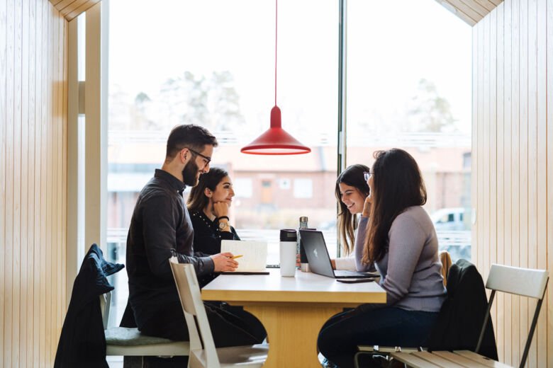 Four students sitting at a table with their laptops, talking and doing group work.