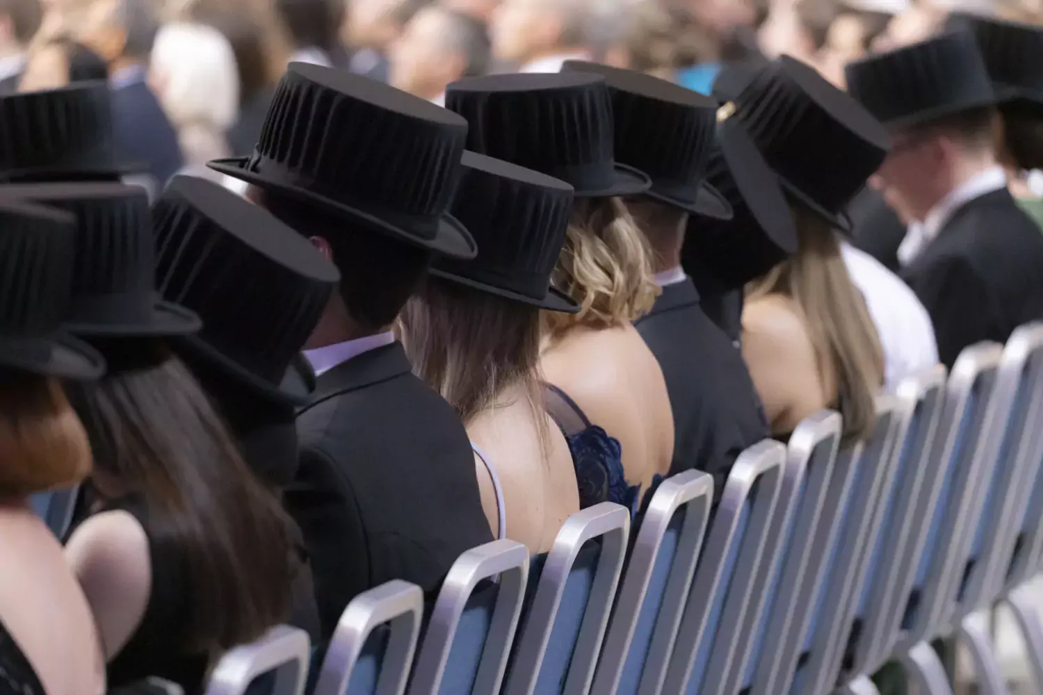 PhD's with their doctoral hats on sits in a row with their backs against the camera.