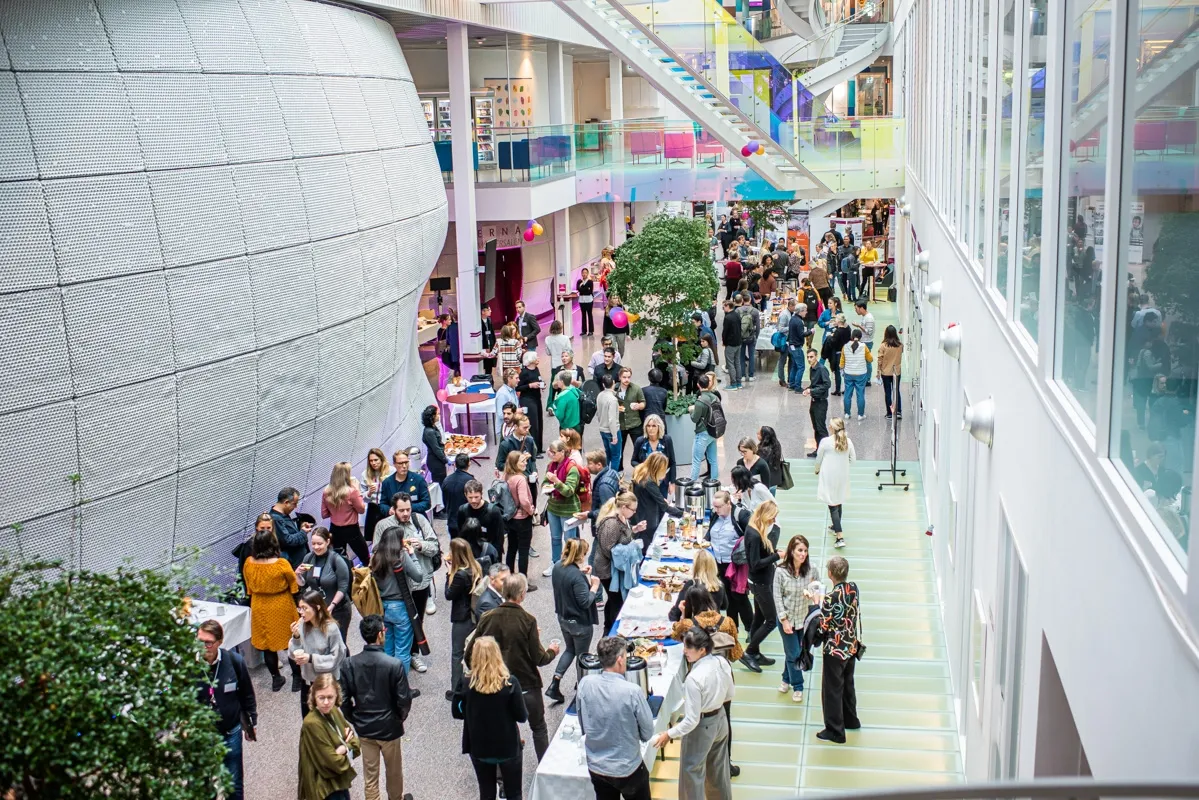 Overview image from the building Neo during the conference. People standing in an open space, chatting.