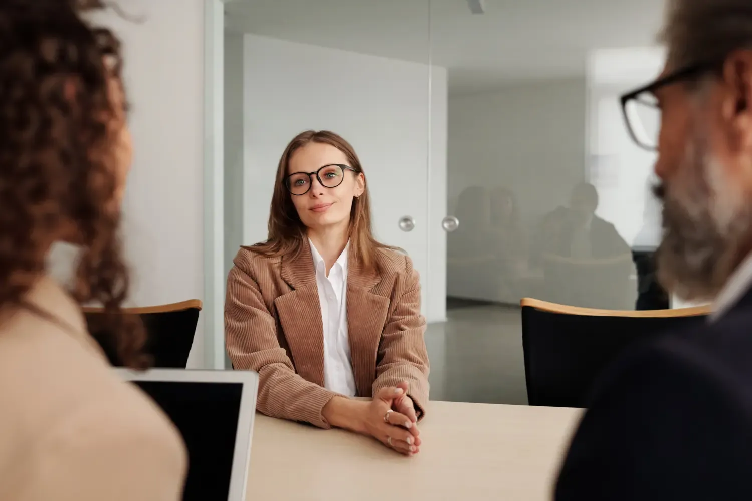 A woman with glasses is sitting opposite two people with notepads in an interview