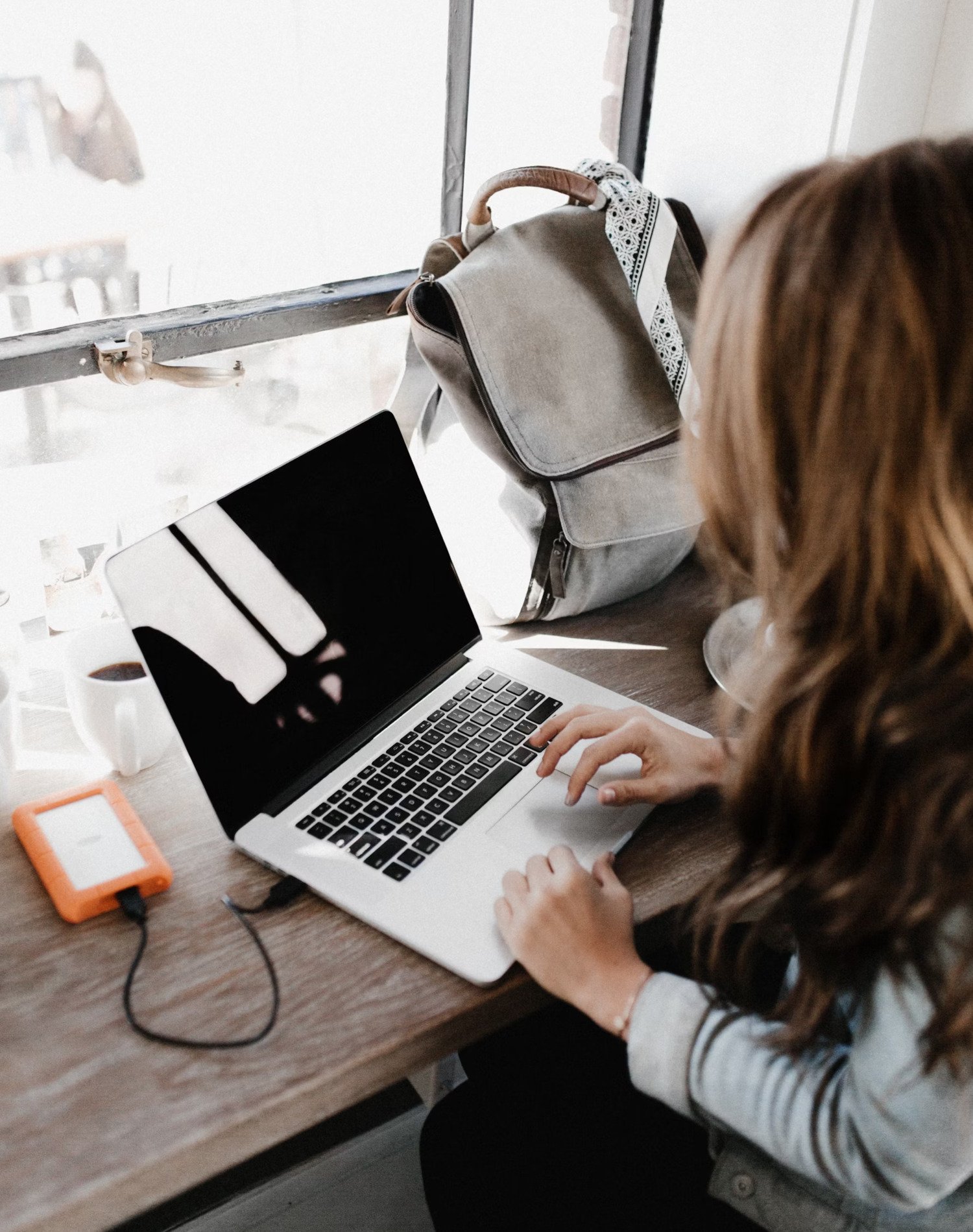 A woman sits with her back to the camera in front of a laptop.