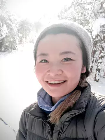 person who identified as female, smiling. There is snow in the background.
