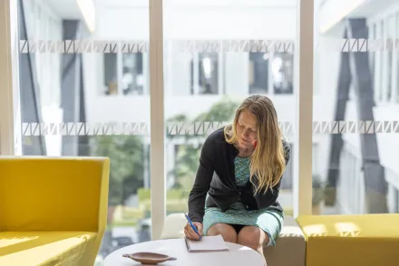Woman sitting on a sofa and writing on a notepad.