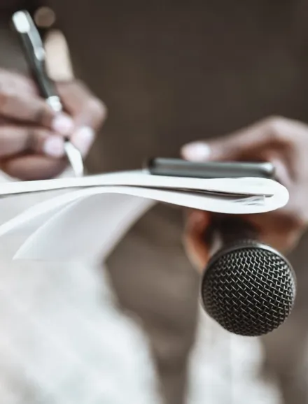 Two hands holding a pen, paper and microphone