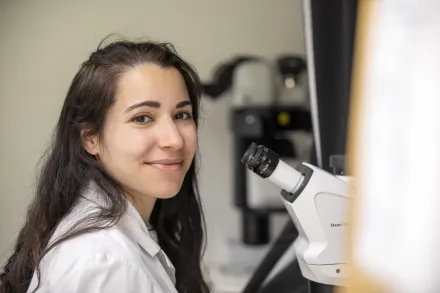 Woman looking up in to the camera from a microscope.