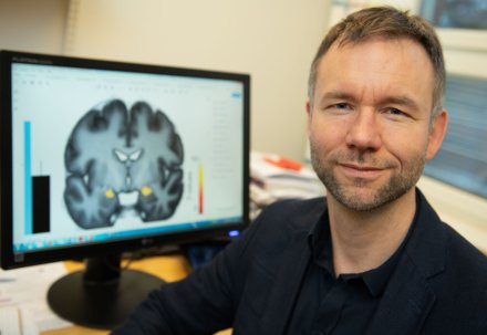 Andreas Olsson in fron av creen with an image of a brain.